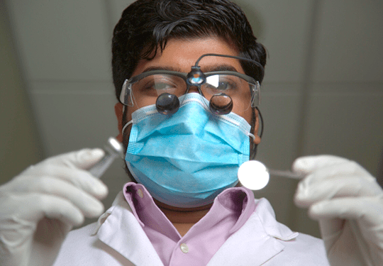 Male doctor wearing goggles and a mask holding dental instruments